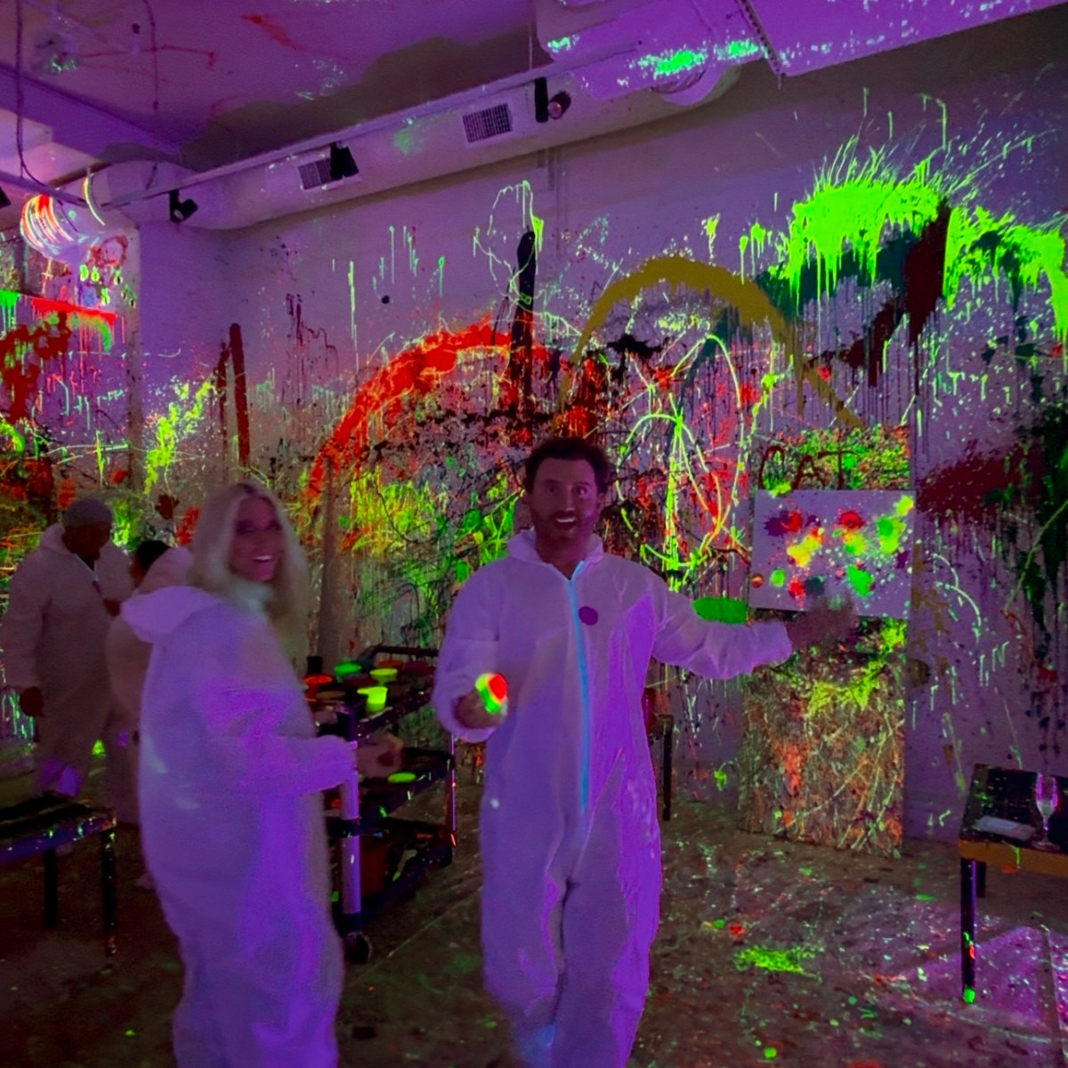People in white suits having fun with neon paint in an art studio.