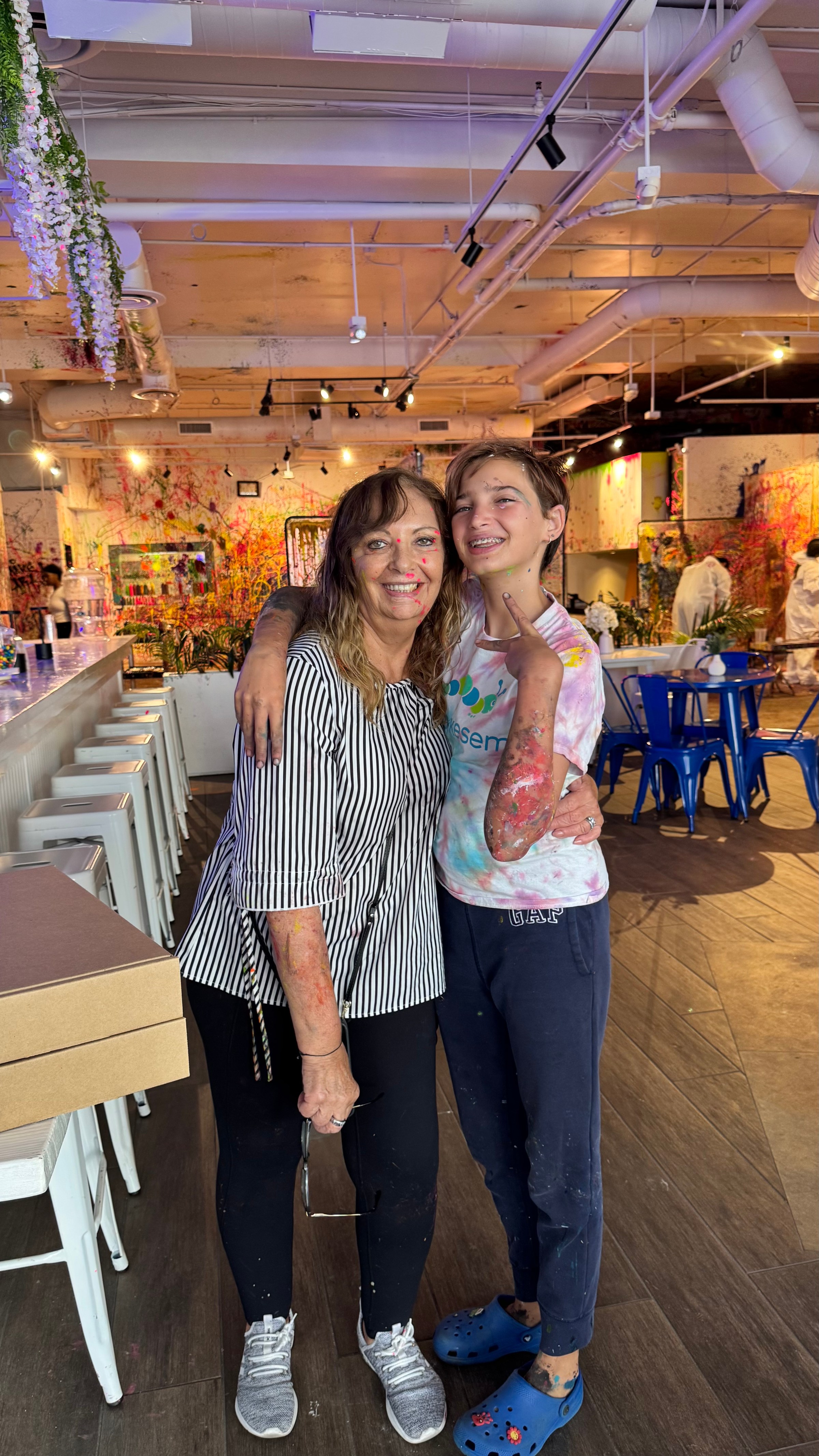 Two people smiling and hugging in a colorful art studio.